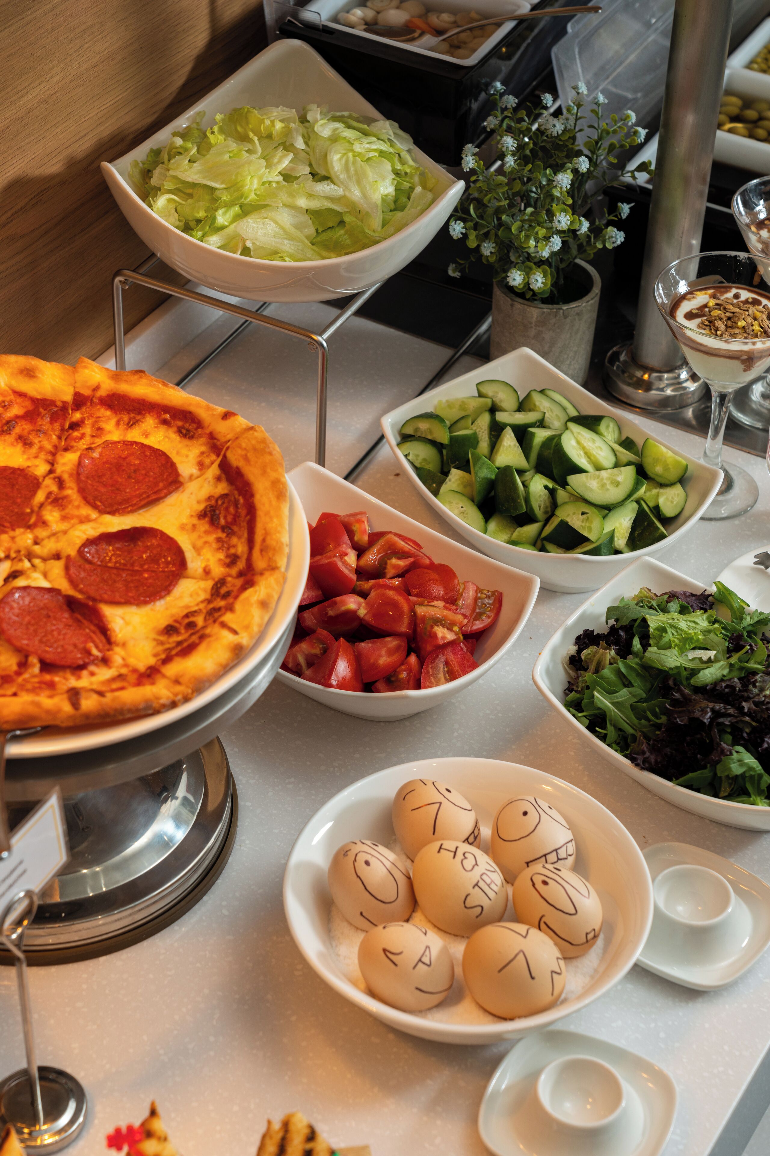 A buffet table with various dishes including pizza, salads, and a bowl of decorated eggs.