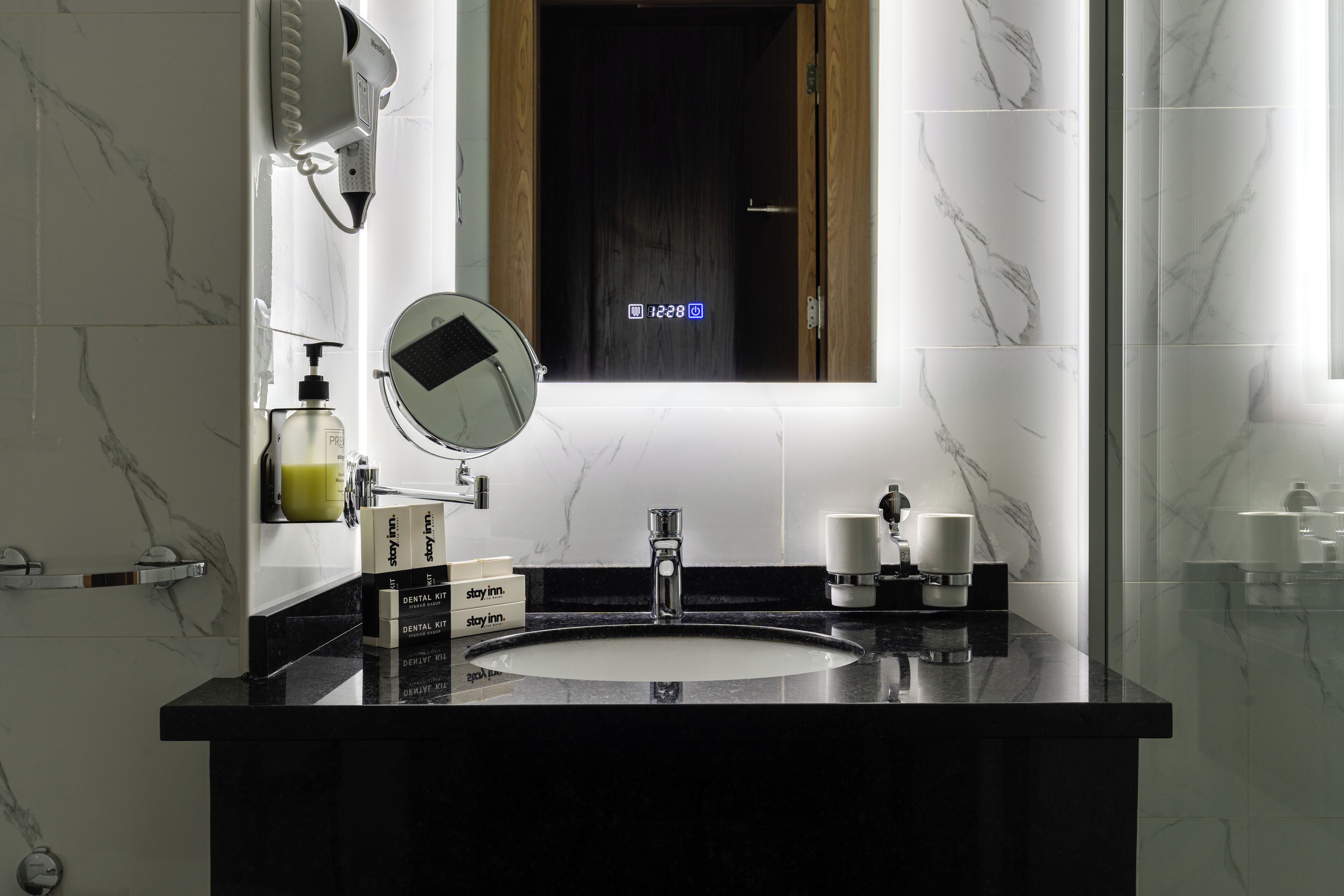 Un baño moderno con un lavabo de mármol negro, un espejo redondo y una pantalla digital sobre el espejo.