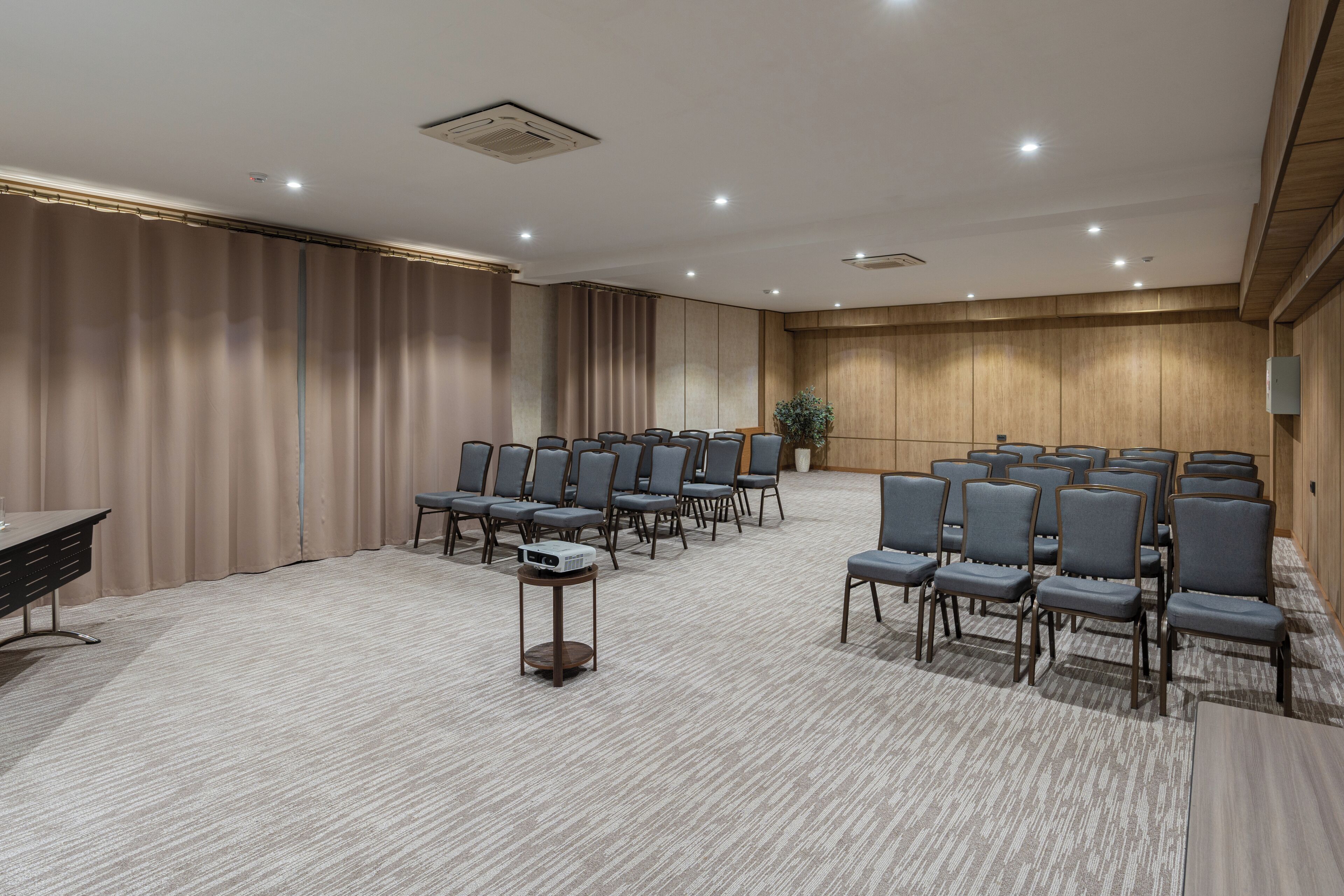 A conference room with rows of chairs, a projector, and a wooden panel wall.