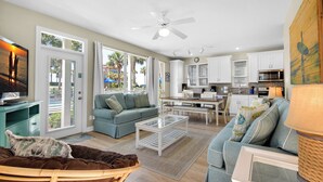 A spacious living room with a sofa, a coffee table, and a TV. There is a kitchen area with cabinets and a microwave. - ⛱️By Beach-Waterfront Villa- Pool-4BR Destiny Beach Villas 11-Beach Oasis (Destin)