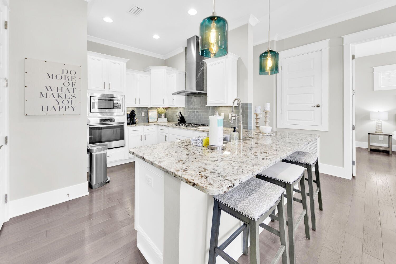 A modern kitchen with white cabinetry, a granite island, stainless steel appliances, and pendant lighting.