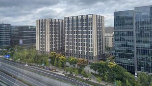 En modern byggnad med en fasad som har ett rutmönster, omgiven av träd och en väl trafikerad väg.