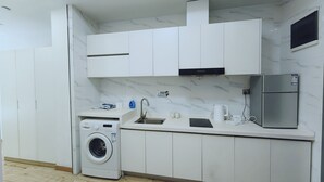 Ett modernt kök med vita skåp, en inbyggd tvättmaskin, en diskho i rostfritt stål och ett kylskåp.