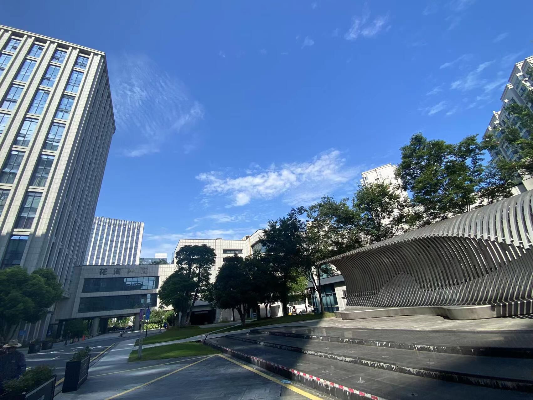 A modern urban plaza with a curved architectural feature, surrounded by tall buildings and trees.