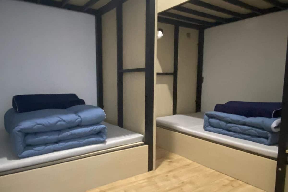 A room with two bunk beds, each with a mattress and a folded blanket.