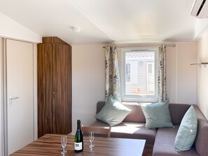 Una habitación moderna con un armario de madera, un sofá con cojines, una mesa con una botella y vasos, y una ventana con cortinas.