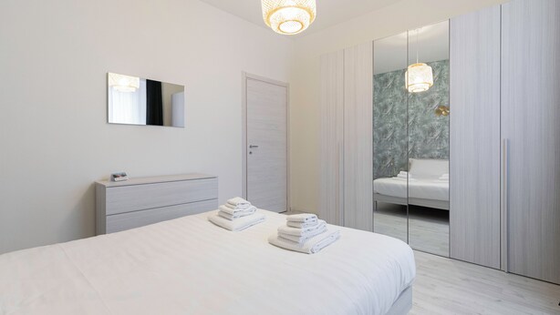 Quarto moderno com cama, mesa de cabeceira, espelho e guarda-roupa.