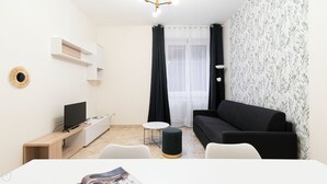 Uma sala de estar moderna e minimalista, com um sofá preto, uma mesinha redonda, uma televisão e um móvel branco.