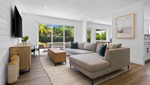 A modern living room with a sectional sofa, a wooden coffee table, and a TV mounted on the wall.