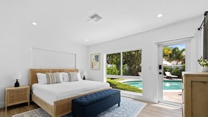A bedroom with a large bed, a bench, a nightstand, and a view of a swimming pool.