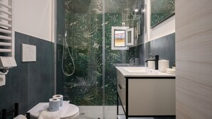 Casa de banho moderna com cabine de chuveiro em vidro, lavatório branco e sanita.
