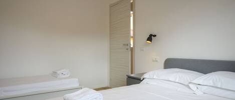A bedroom with a bed, a bedside table, a nightstand, and a door leading to another room.