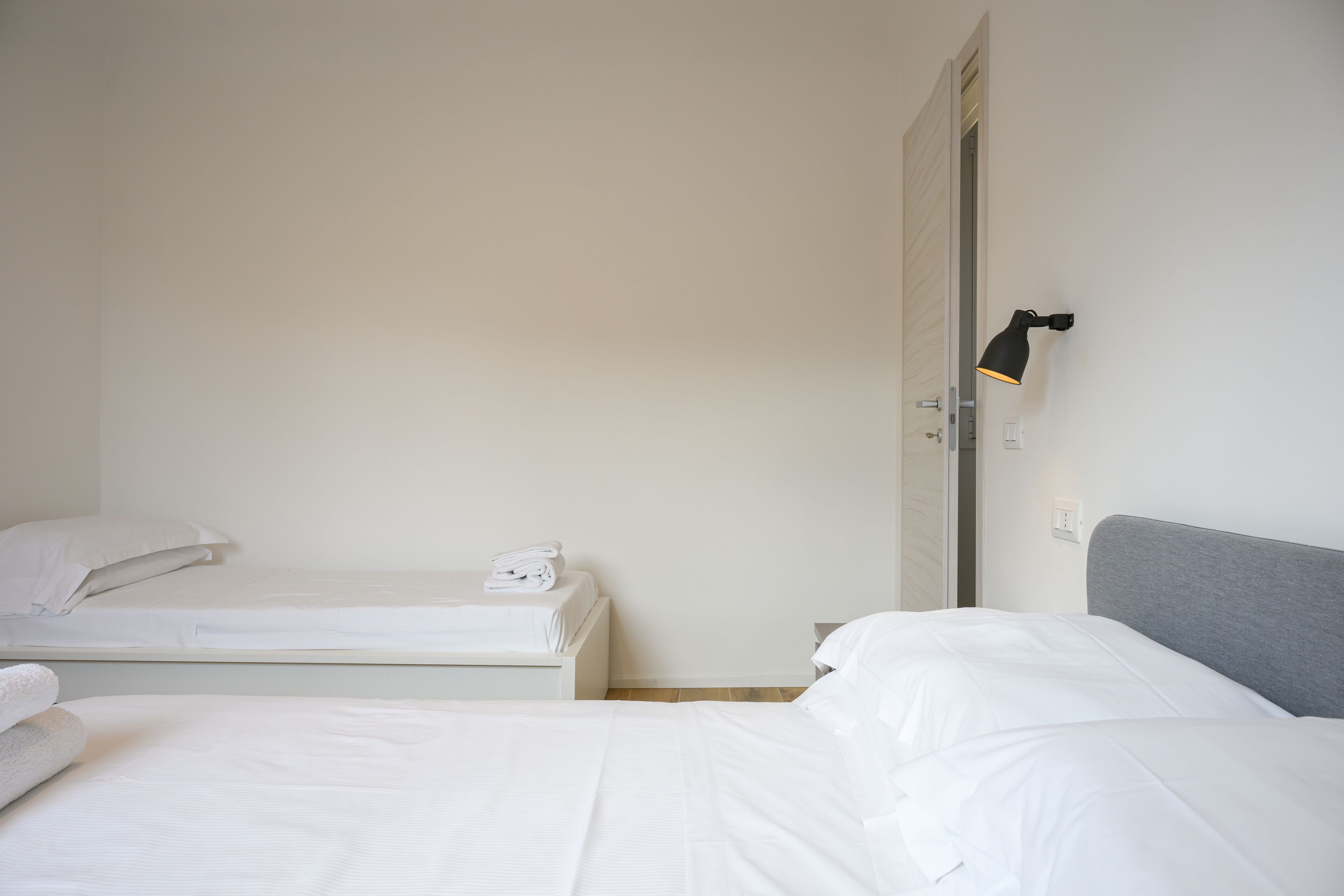 Een hotelkamer met twee bedden, een grijze hoofdbord en een wandlamp.