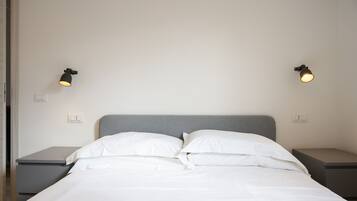 Un lit bien fait, avec du linge de lit blanc et des oreillers, deux tables de chevet avec des lampes noires et un mur blanc uni.
