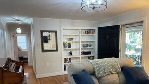 A living room with a piano, a bookshelf, a sofa with cushions, and a door leading to a balcony.
