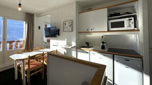 A compact kitchen with a microwave, sink, and dishwasher. There is a dining area with a table and chairs. - 10m from ski slopes, 7th floor, view mountain, balcony, tv, 25m², Les Menuires (Les Menuires)