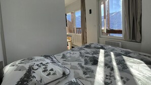 A bedroom with a bed, a window with curtains, and a view of a balcony. - 10m from ski slopes, 7th floor, view mountain, balcony, tv, 25m², Les Menuires (Les Menuires)