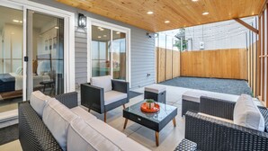 A covered patio area with wicker furniture, a glass coffee table, and sliding glass doors leading to an interior space. - Pacific Northwest Retreat Duplex 3min from Seattle by RedAwning (Tukwila)