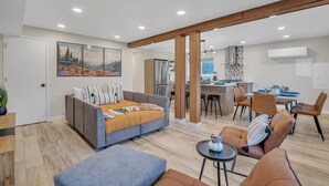 A modern living room with a grey sofa, a blue ottoman, and a dining area with brown chairs and a table. - Pacific Northwest Retreat Duplex 3min from Seattle by RedAwning (Tukwila)