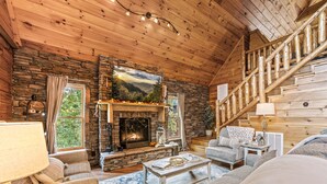 A cozy log cabin interior with a stone fireplace, wooden staircase, and comfortable seating areas. - *Relaxing 2BDR Getaway! HOT TUB + Arcade + XBox* (Sevierville)
