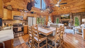 A rustic cabin interior with wooden walls, a stone fireplace, a dining area with wooden chairs, and a ceiling fan. - *Relaxing 2BDR Getaway! HOT TUB + Arcade + XBox* (Sevierville)