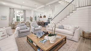 A spacious living room with a high ceiling, a staircase, and a dining area.