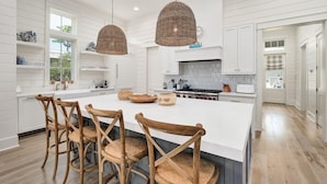 A spacious kitchen with a large island, wooden chairs, and hanging wicker light fixtures.