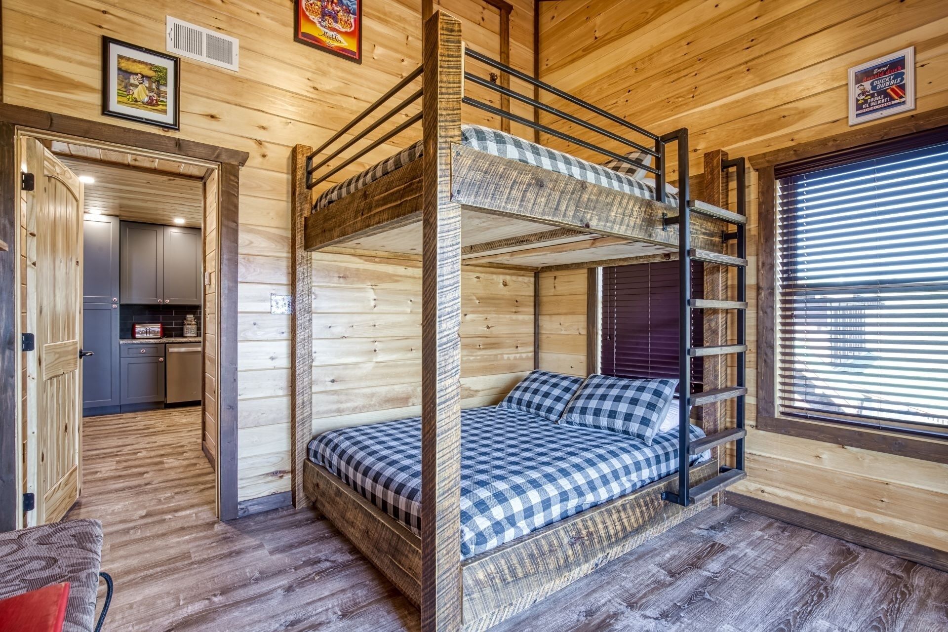 A bunk bed room with a kitchen area, wooden walls, and a window with blinds.