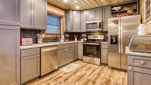 Una cocina moderna con electrodomésticos de acero inoxidable, gabinetes grises y techo de madera.