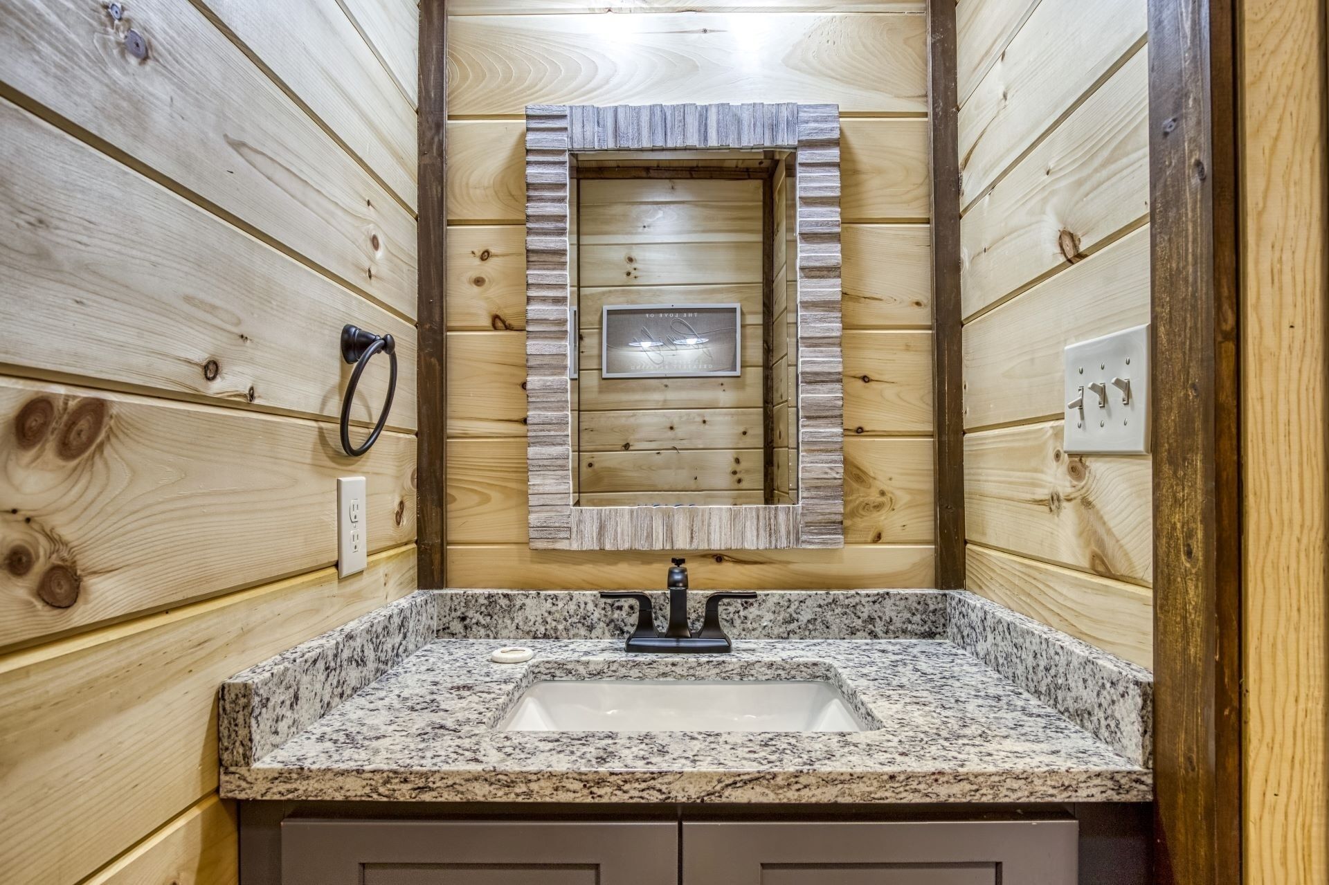 A bathroom with a granite sink, wooden walls, a mirror, and a towel ring.