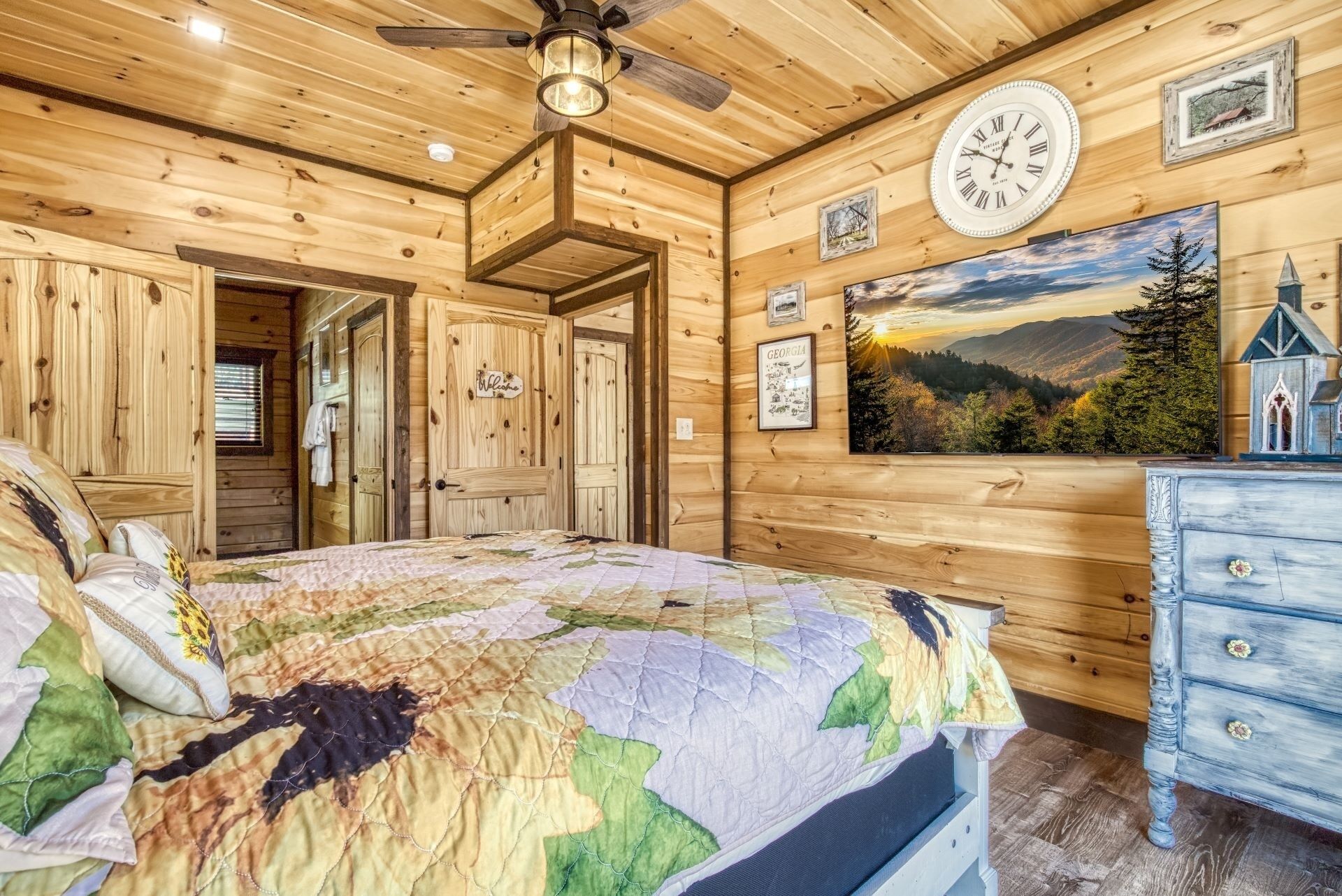 A wooden cabin bedroom with a bed, a clock, and a scenic painting.