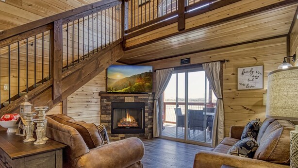 Interior acogedor de una cabaña con chimenea de piedra, mobiliario de madera y un balcón con vistas panorámicas.