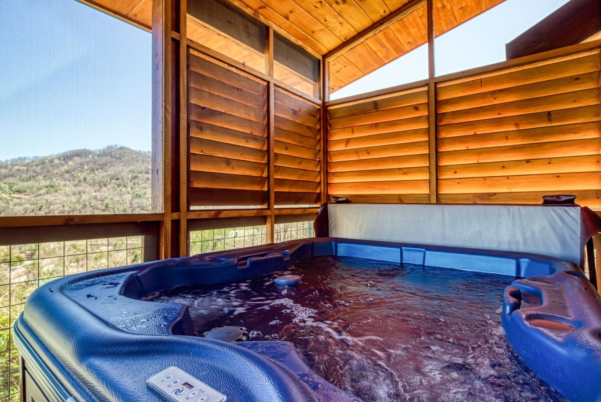 Un jacuzzi con panel de control, rodeado de paredes de madera y ventanas amplias que ofrecen vistas a un paisaje montañoso.