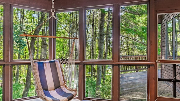 A room with large windows, a hanging chair, and a wooden deck.