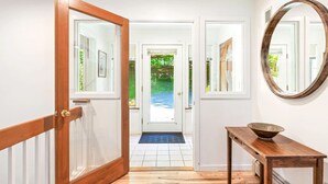 A hallway with a wooden door leading to a room, a round mirror on the wall, and a wooden table with a bowl.