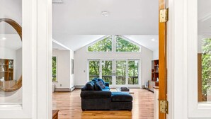 A spacious living room with a large window, a dark sofa, and a wooden floor.