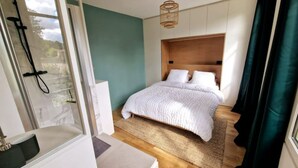Un dormitorio con cama, cabecero de madera, ventana con cortinas y zona de ducha.