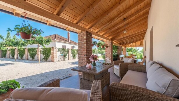 Un espace extérieur aménagé en terrasse, avec des meubles en osier, des jardinières suspendues et une vue sur une maison en arrière-plan.