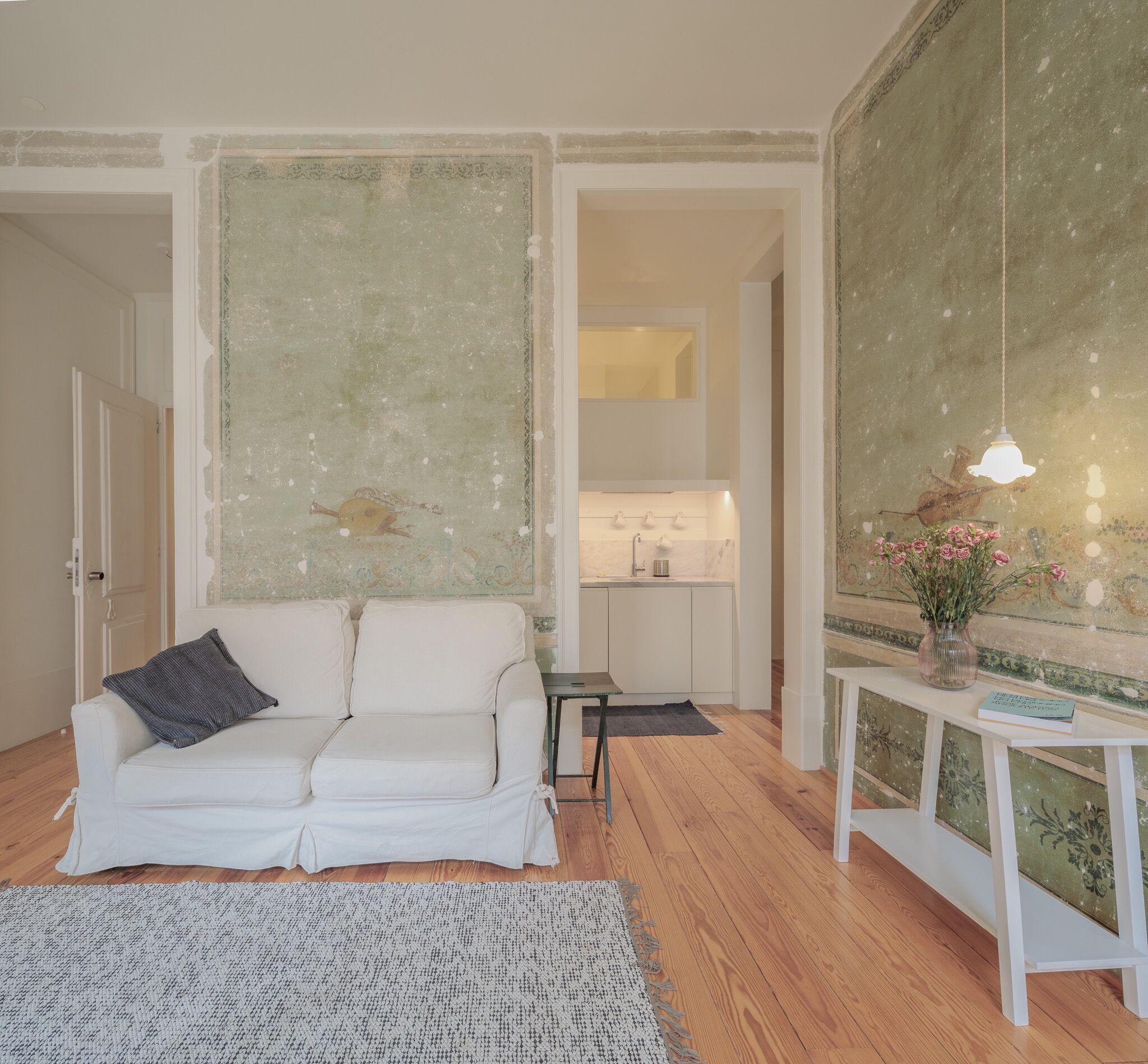 Een woonkamer met een witte bank, een klein tafeltje, een vloerkleed en een muur met een decoratief patroon.