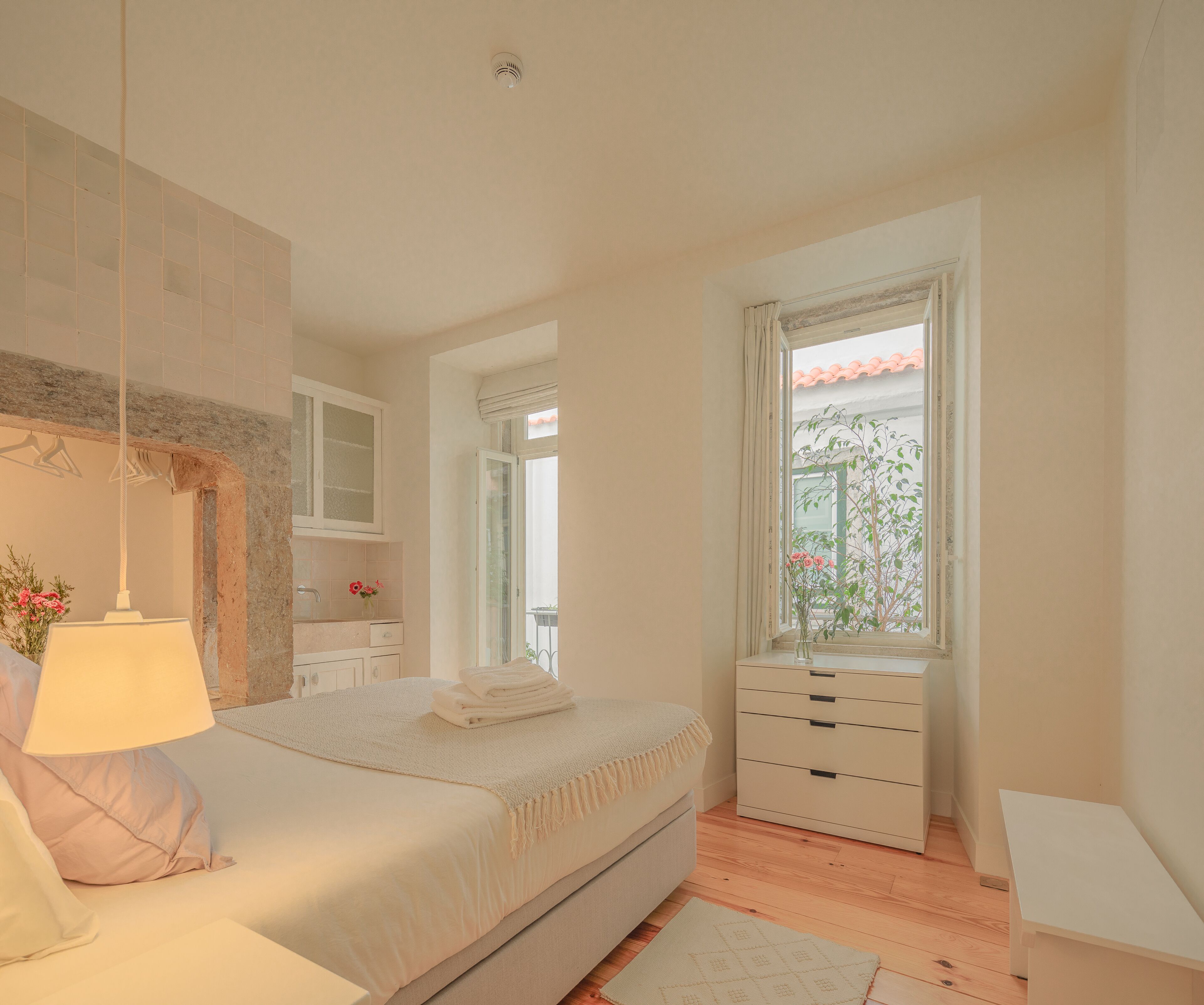Un dormitorio con cama, mesita de noche, lámpara, cómoda y ventana con vistas a zonas verdes.