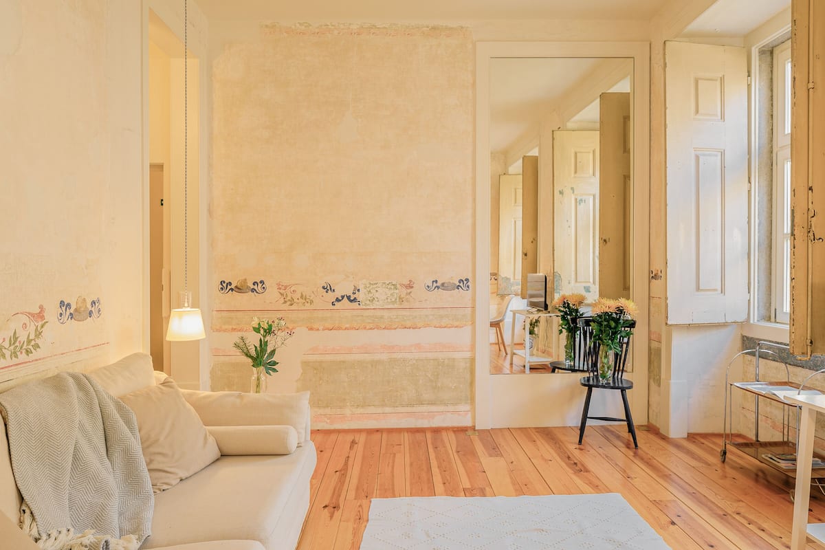 Een gezellige woonkamer met een houten vloer, een beige bank, een kleine tafel met een bloemetjesvaas, en een spiegel die de kamer weerkaatst.