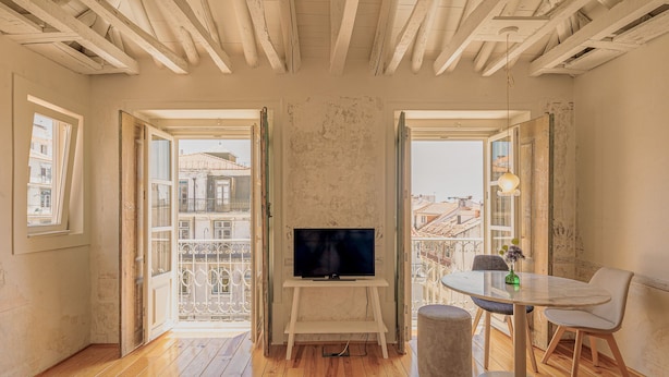 Een kamer met houten vloeren, een televisie op een standaard, een ronde tafel met stoelen en grote ramen met balkons.