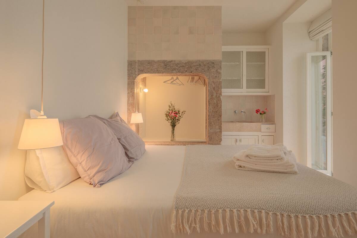 Een slaapkamer met een bed, nachtkastje, lamp en uitzicht op de badkamer.