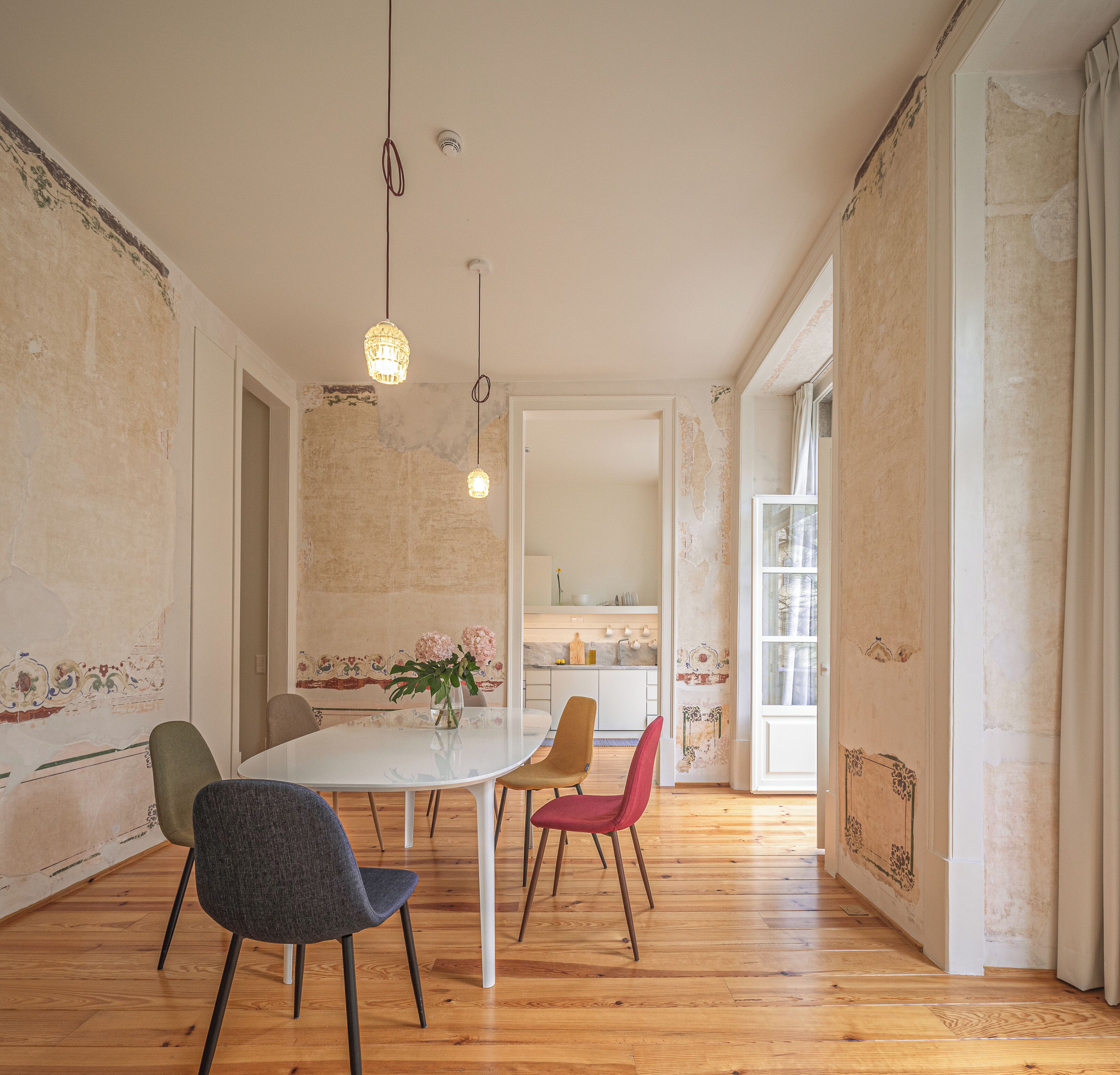 A dining area with a white table, three chairs, hanging pendant lights, and a view into the kitchen.