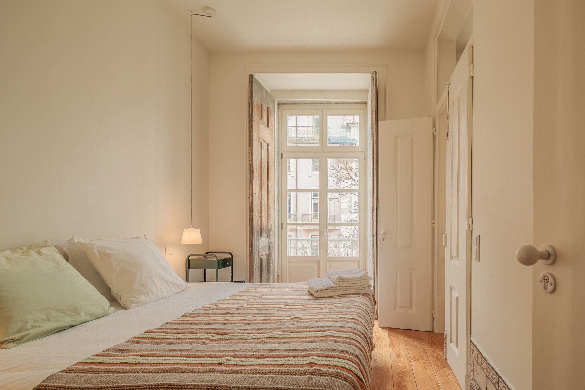 Un dormitorio con una cama, una mesita de noche, una lámpara y una puerta que da a un balcón.