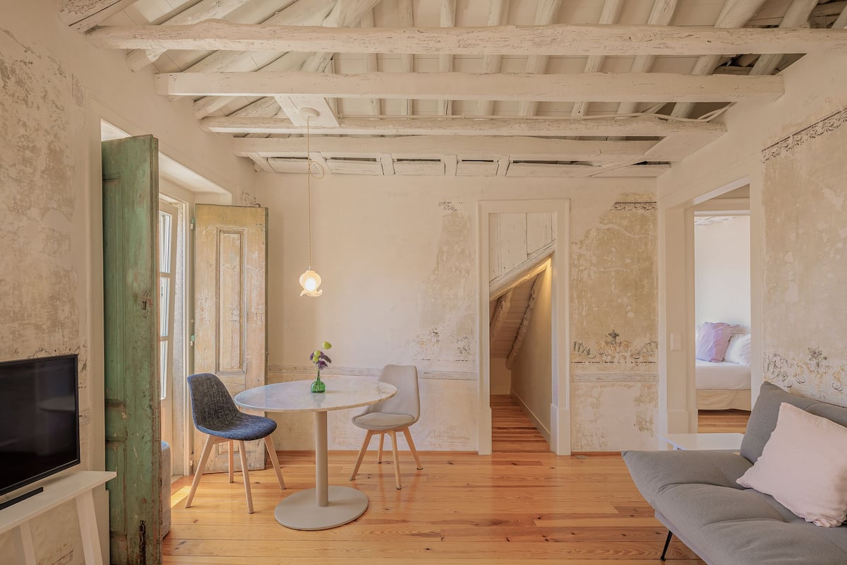 Een kamer met een houten plafond, een eettafel met twee stoelen, een bank en een televisie op een dressoir.
