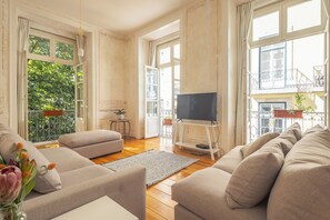 A living room with a sofa, a TV on a stand, a small table, and a balcony with plants. - Antiga Casa Pessoa (Lisbon)