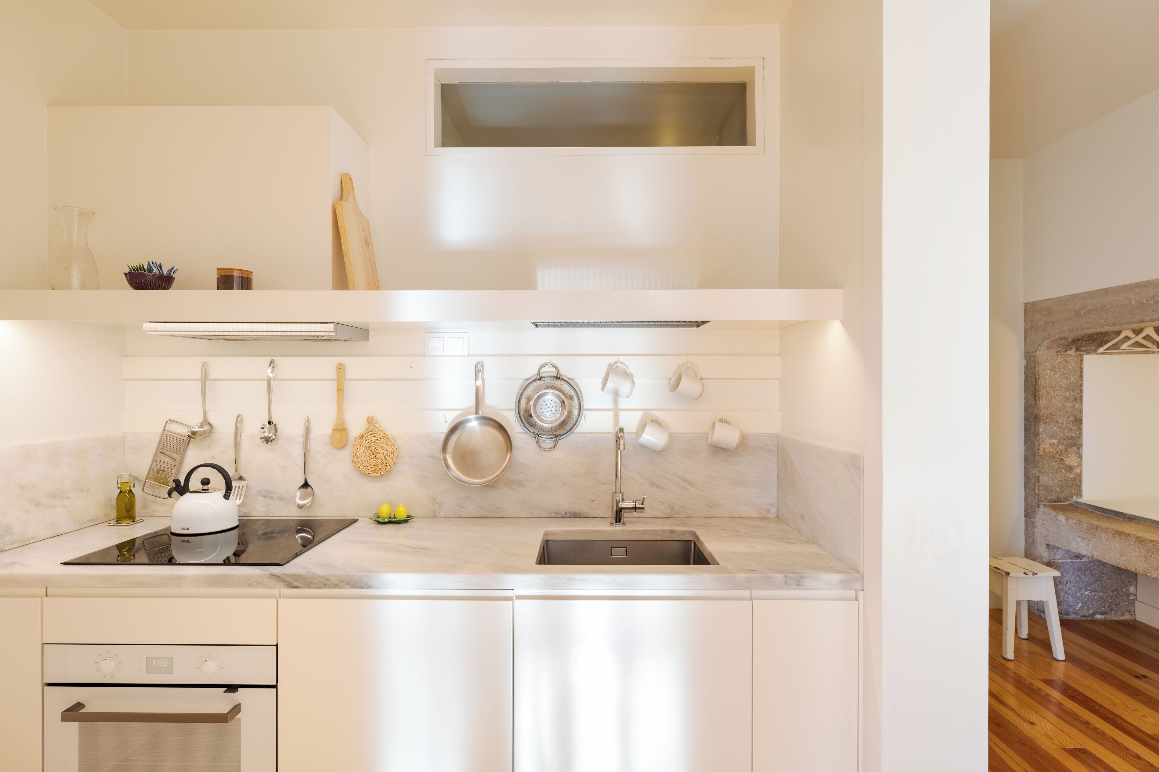 A modern kitchen with white cabinetry, a built-in oven, a stovetop, and a variety of utensils and cookware hanging on the wall.