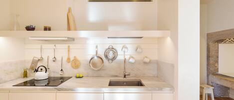 A modern kitchen with white cabinetry, a built-in oven, a stovetop, and a variety of utensils and cookware hanging on the wall.
