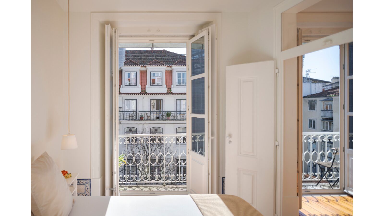 Un dormitorio con cama, mesita de noche, lámpara y vistas a un balcón con barandilla.